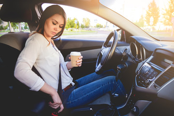 Young beautiful woman driving a car seat belt with a cup of coffee in hand