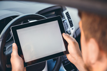 A young man with a tablet in his hand at the wheel of the car. Multitasking. Safe driving concep