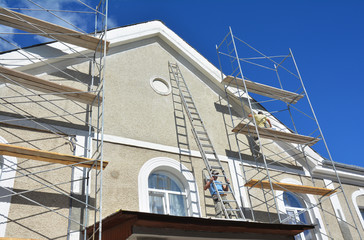 Painting and Plastering Exterior House Scaffolding Wall. Facade Thermal Insulation and Painting Works During Exterior Renovations. Builder Worker Plastering House Facade.