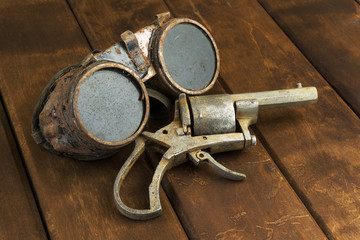 Old rusty steampunk goggles with a revolver on wooden desk