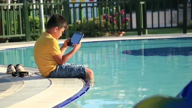 Young boy using digital tablet near the pool