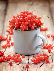 Fresh organic red currants in a cup on the old wooden table.