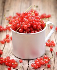 Fresh organic red currants in a cup on the old wooden table.