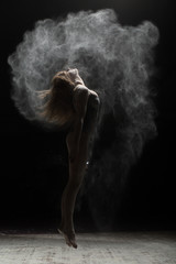 Flexible woman jumping and sprinkle flour on black background