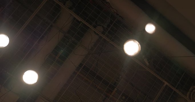 View to the dark ceiling with metal mesh, pipes and small lamps hanging on metal sticks