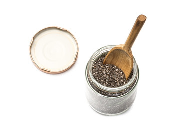 Chia seeds in a glass jar with a wooden spoon in it and the lid next to it seen from above on white background