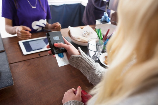 Over shoulder view of female customer paying with credit card reader in cafe