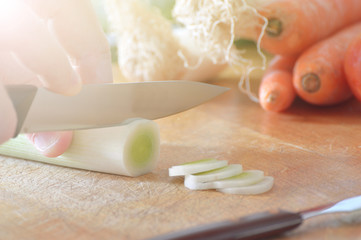 Hands cutting some leeks on a wooden table while cooking in a rustic kitchen.