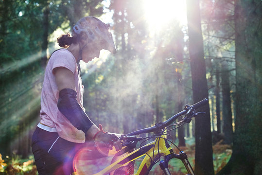 Female mountain biker standing in sunbeam with head down, Forest of Dean, Bristol, UK