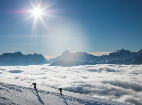 Two climbers on a snowy slope above a sea of fog in an alpine valley, Alps, Canton Wallis, Switzerland