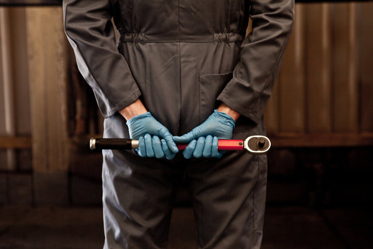 Male mechanic holding socket wrench behind back, rear view, mid section