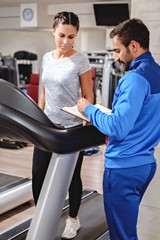 Fitness instructor writing program to his client on a treadmill