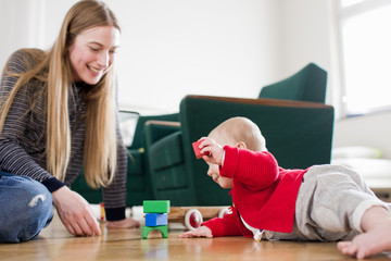 Woman and baby daughter play with building blocks on living room floor