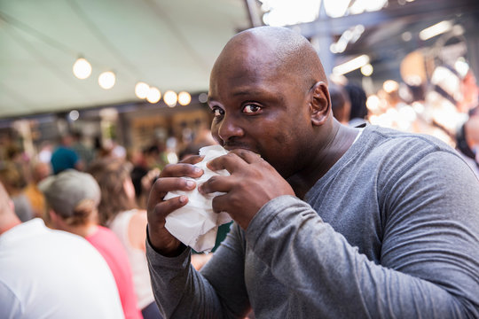 Male Customer Eating Burger At Cooperative Food Market Stall