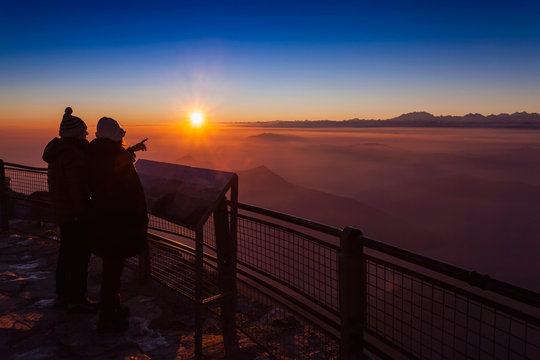 Senior hiking couple looking out over mountain valley mist at sunset, Monte Generoso,Ticino, Switzerland
