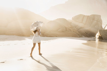 Rear view of woman strolling with parasol on sunlit beach, Cape Town, South Africa