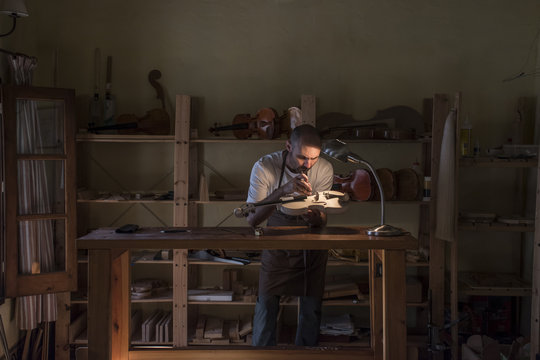Luthier examining the sound post of an unvarnished violin in his workshop