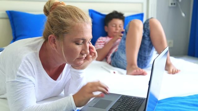 Mother and son browsing internet in a laptop and smart phone in the bedroom at home