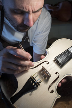 Luthier examining the sound post of an unvarnished violin in his workshop