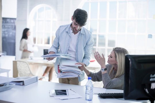 Male and female designers selecting from stack of paperwork at design studio meeting
