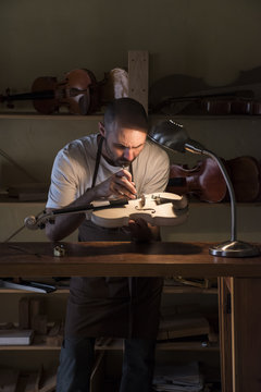 Luthier examining the sound post of an unvarnished violin in his workshop