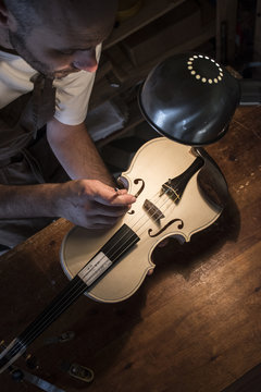 Luthier examining the sound post of an unvarnished violin in his workshop