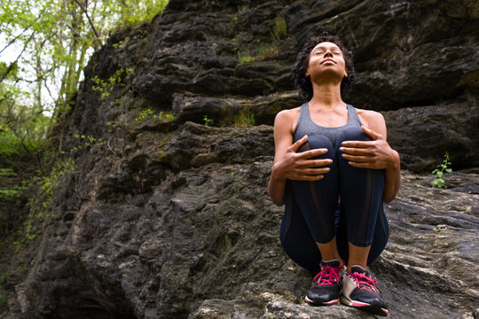 Woman sitting hugging knees on rock meditating