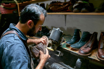 Male cobbler in traditional shoe workshop inspecting boot