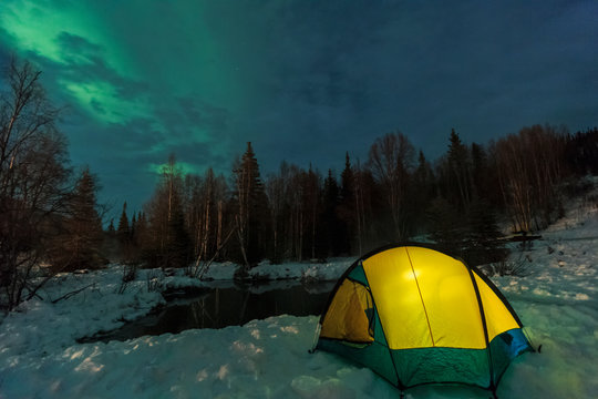 Aurora borealis, Northern Lights above tent lit up with lantern, near Chena Resort, near Fairbanks, Alaska