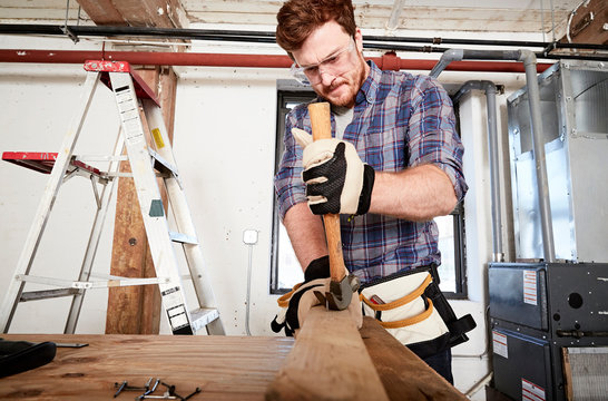 Carpenter in workshop removing nails form timber using hammer