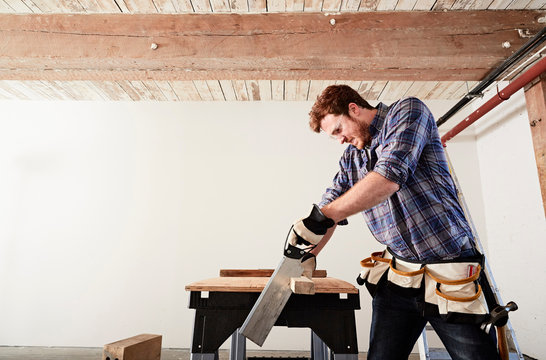 Carpenter in workshop sawing timber