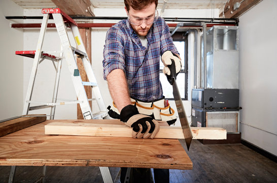 Carpenter in workshop sawing timber