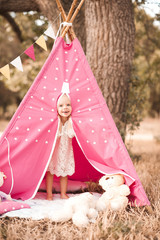 Fototapeta na wymiar Laughing baby girl playing in wigwam with toys outdoors. Looking at camera. Playful