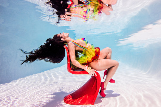 Woman underwater in swimming pool sitting on red plastic chair
