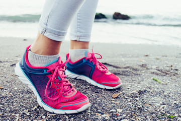 Close-up of female legs in sneakers and jeans on the beach near