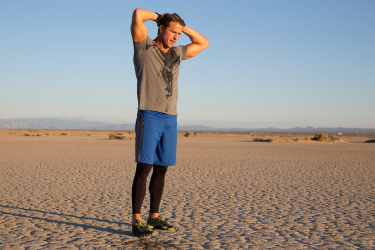 Man training, sweating with hands behind head on dry lake bed, El Mirage, California, USA