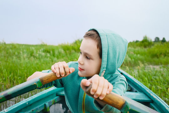 Boy Rowing A Wooden Boat. Child Controls Rowing Boat Near The Shore. Closeup