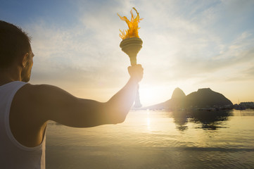Torchbearer athlete standing with sport torch against a scenic sunrise view of Sugarloaf Mountain and Botafogo Bay in Rio de Janeiro, Brazil - obrazy, fototapety, plakaty