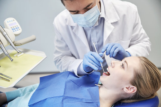 male dentist in mask checking female patient teeth