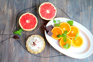 Grapefruit halves and orange slices with mint leaves and chocolate and creamy dessert on a wooden table