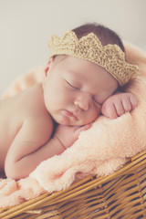 Adorable little guy,in a beige knitted crown,tucked under his legs and put the handle under his head,sound asleep on the soft beige blanket in a large wicker basket high,sweet sleeping newborn baby