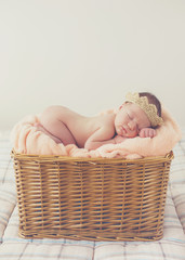 Adorable little guy,in a beige knitted crown,tucked under his legs and put the handle under his head,sound asleep on the soft beige blanket in a large wicker basket high,sweet sleeping newborn baby