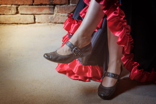 Close up view of legs of woman sitting on a chair and dressed in costume of Flamenco dancer. The photo has deliberately darkened edges. Horizontally. 