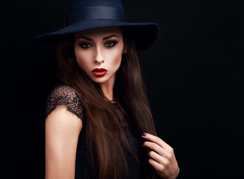 Mysterious makeup woman in fashion hat looking expressive on bla