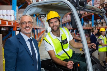 Worker driving forklift looking at camera with businessman
