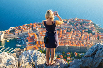 Female traveller make a panoramic photo of the old city of Dubrovnik from the mountain to her phone...