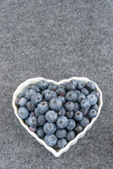 Fresh blueberries in a white heart shaped bowl, on gray background
