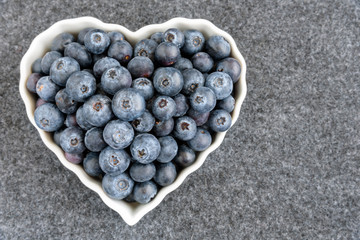 Fresh blueberries in a white heart shaped bowl, on gray background
