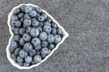 Fresh blueberries in a white heart shaped bowl, on gray background
