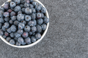 Fresh blueberries in a white bowl, on gray background
